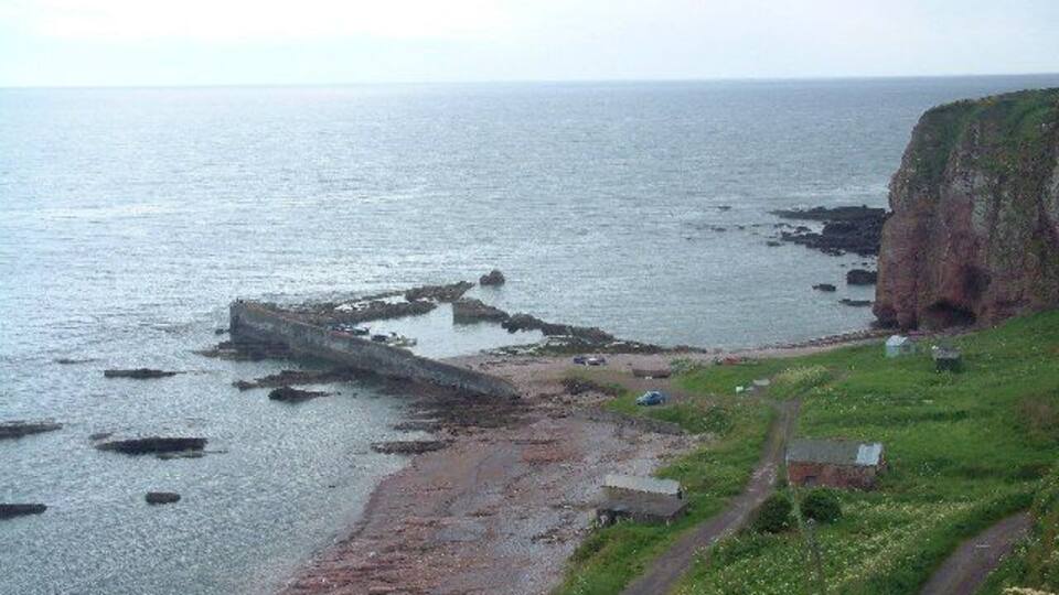 A coastal landscape with a cliff, a rocky breakwater, and a grassy area with a path.