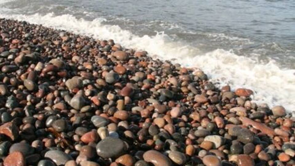 A pebbly beach with waves crashing onto the shore and cliffs in the background.