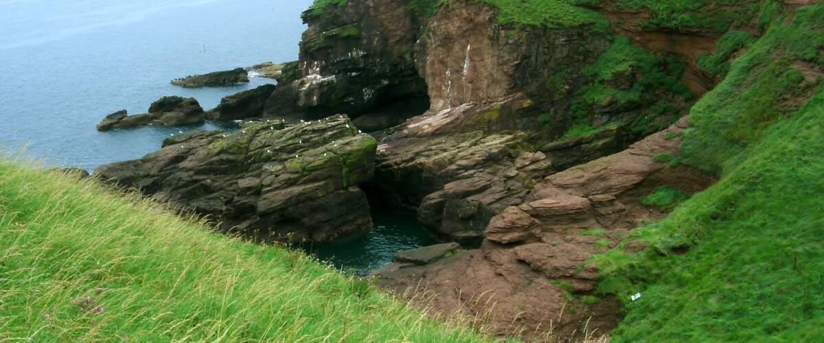 Een kustlandschap met rotsachtige kliffen, grasheuvels en uitzicht op zee.