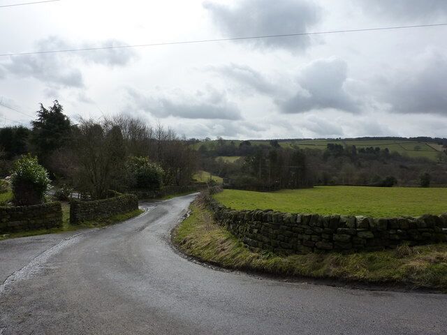 Oaks Lane at Brockhurst Farm A sharp bend in the road. Looking south, and nearing the bottom of the valley, where the thin strip of woodland has a stream running through, Hodgelane Brook