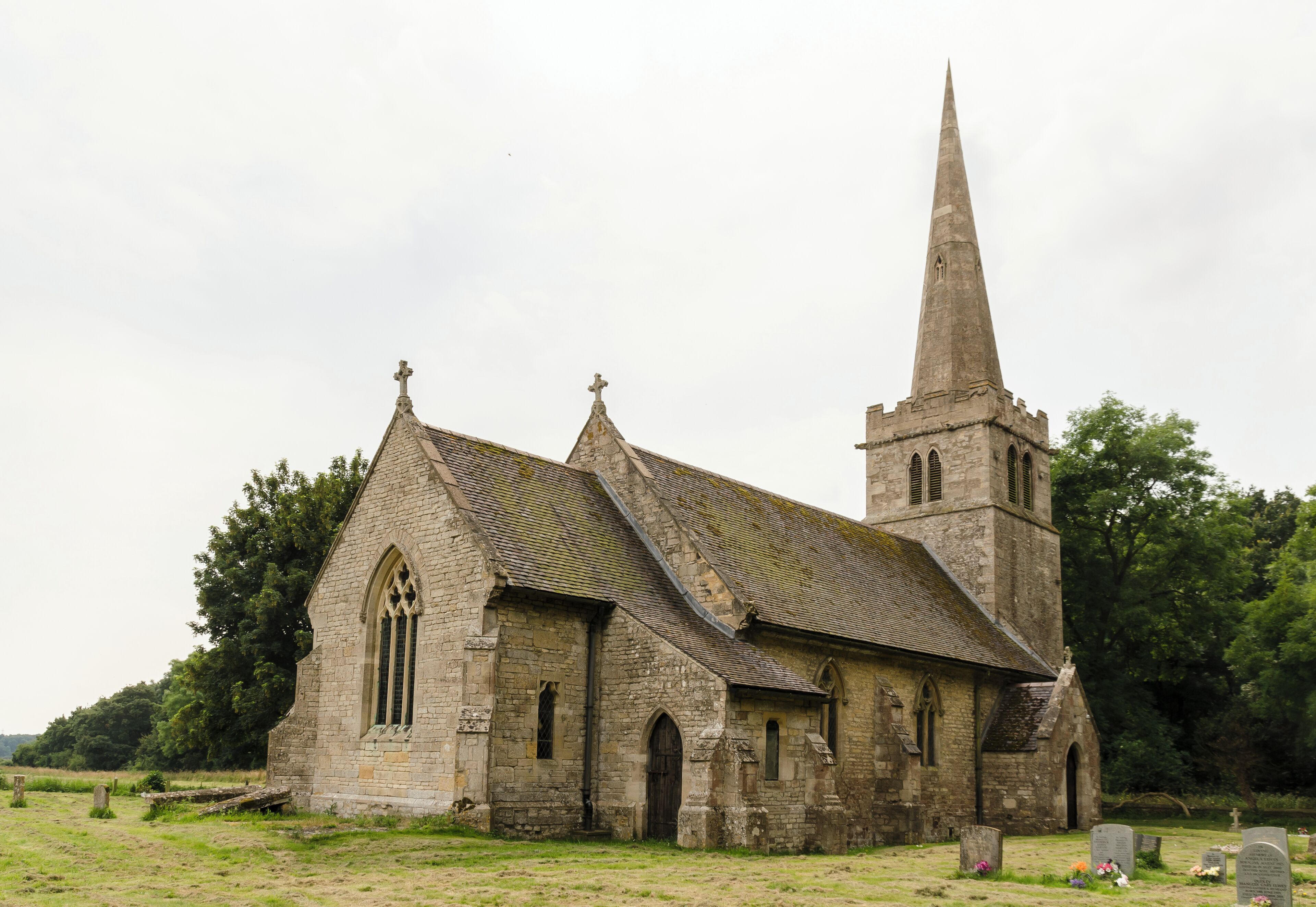 An old stone church with a tall spire and a graveyard in the foreground.