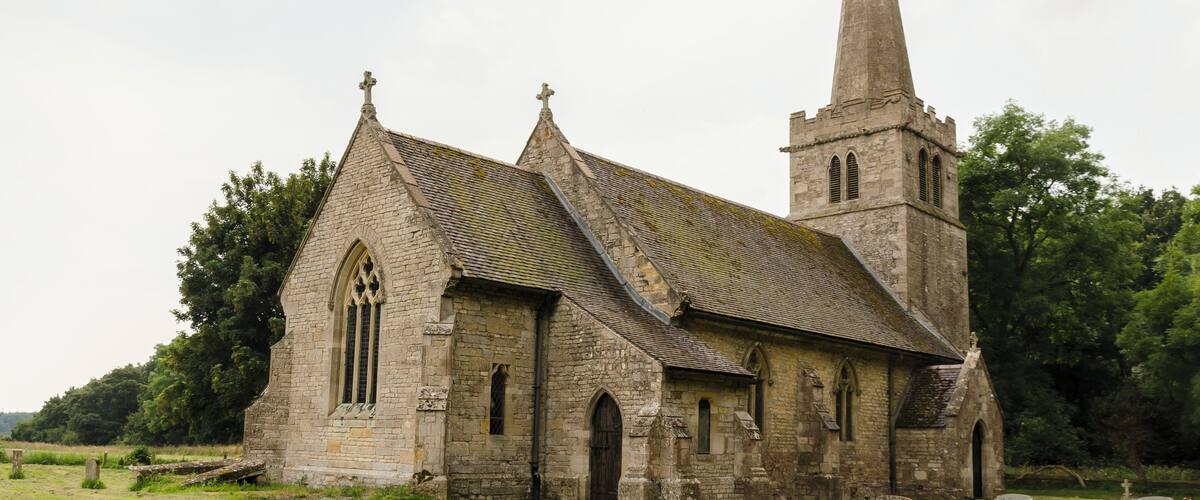 An old stone church with a tall spire and a graveyard in the foreground.