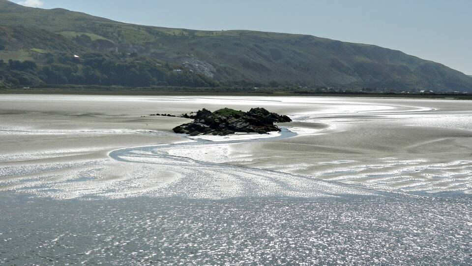 A rocky island in a shallow, reflective water body with a mountainous backdrop.