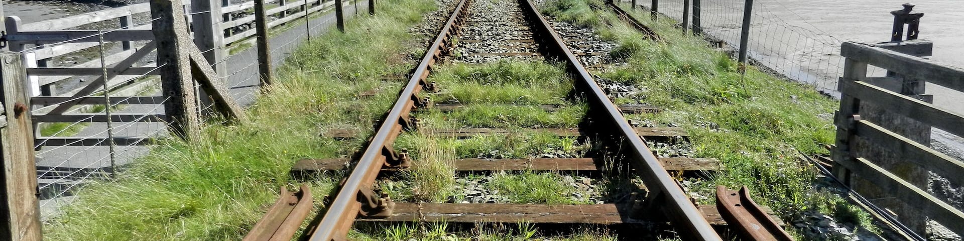 A railway track leading to a bridge over a body of water, surrounded by hills.