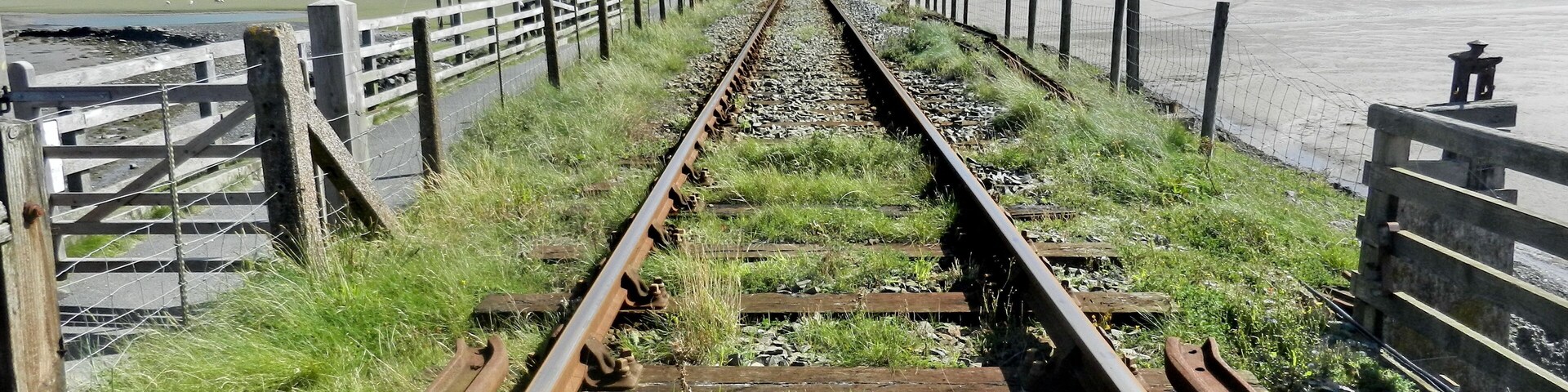 Vías de tren que conducen a un puente sobre un cuerpo de agua, rodeado de colinas.