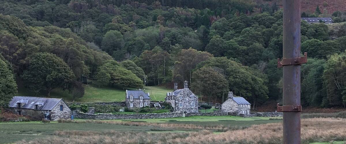 A rural landscape with a river, stone houses, and a hill in the background.
