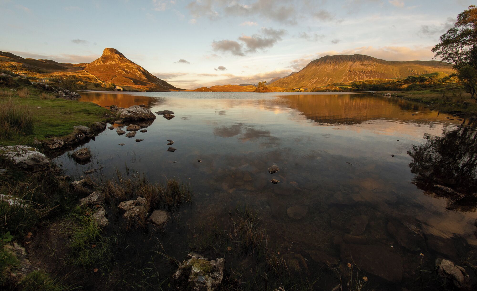 A calm lake surrounded by hills and a small house near the water's edge.