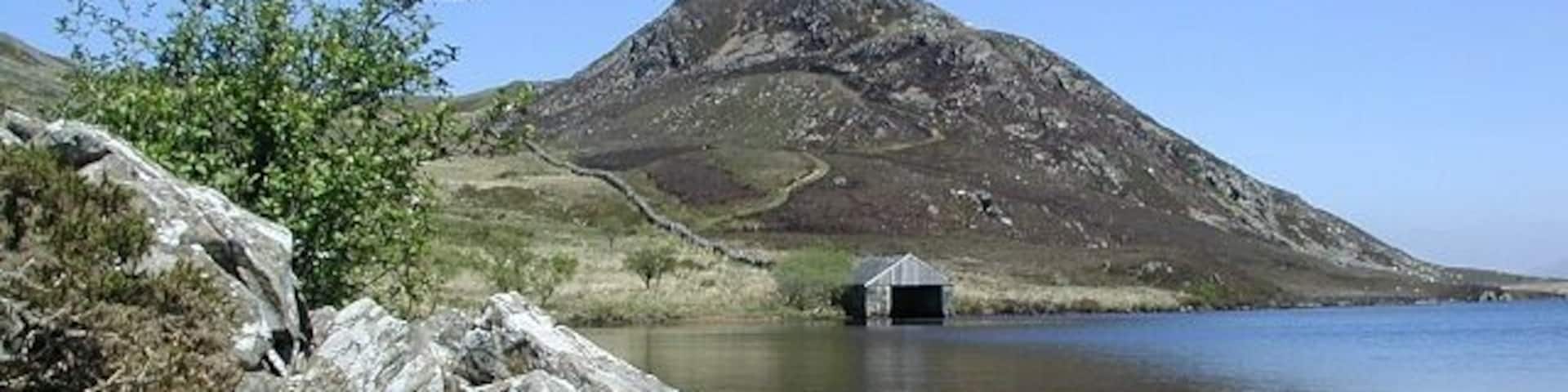 A calm lake with rocky shores, a small hut, and a mountain in the background.