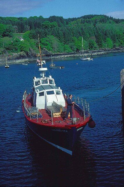 A red boat docked at a pier with a forested hill in the background.