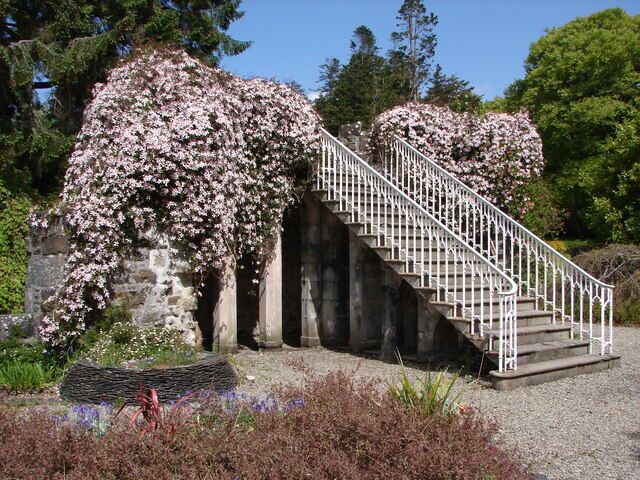 A stone staircase with white railings leading up to a stone archway, surrounded by blooming cherry trees.