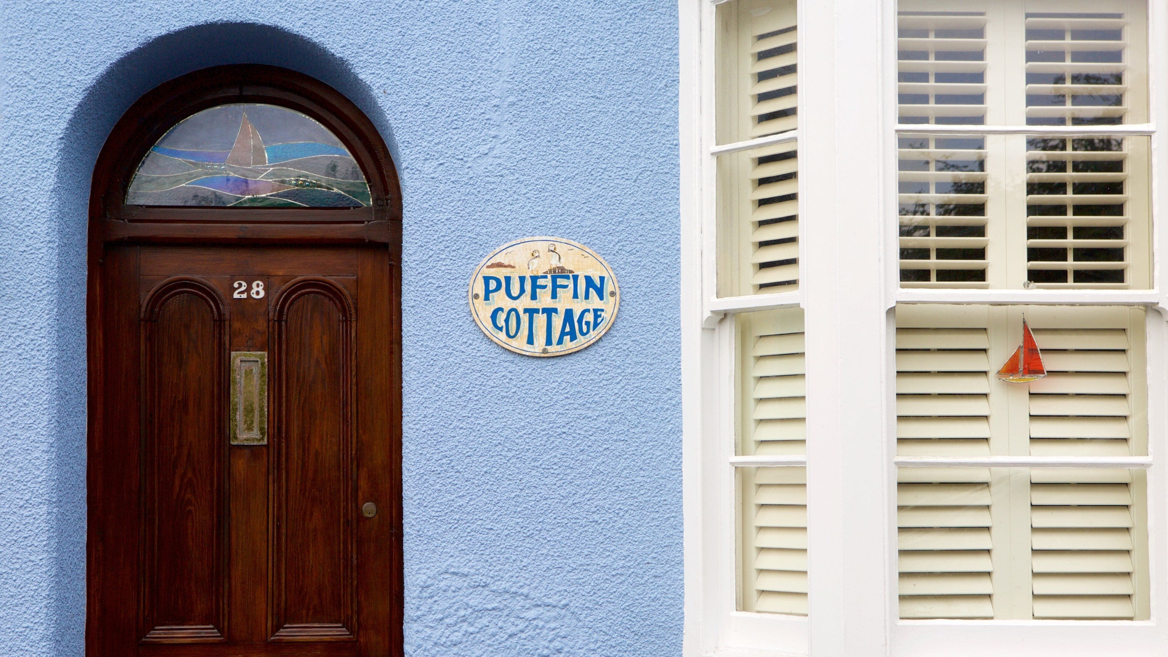 A wooden door with the number 28, a blue wall, and a sign that reads "PUFFIN COTTAGE".