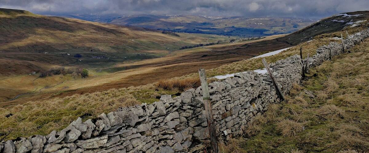 A stone wall, rolling hills, and a cloudy sky.