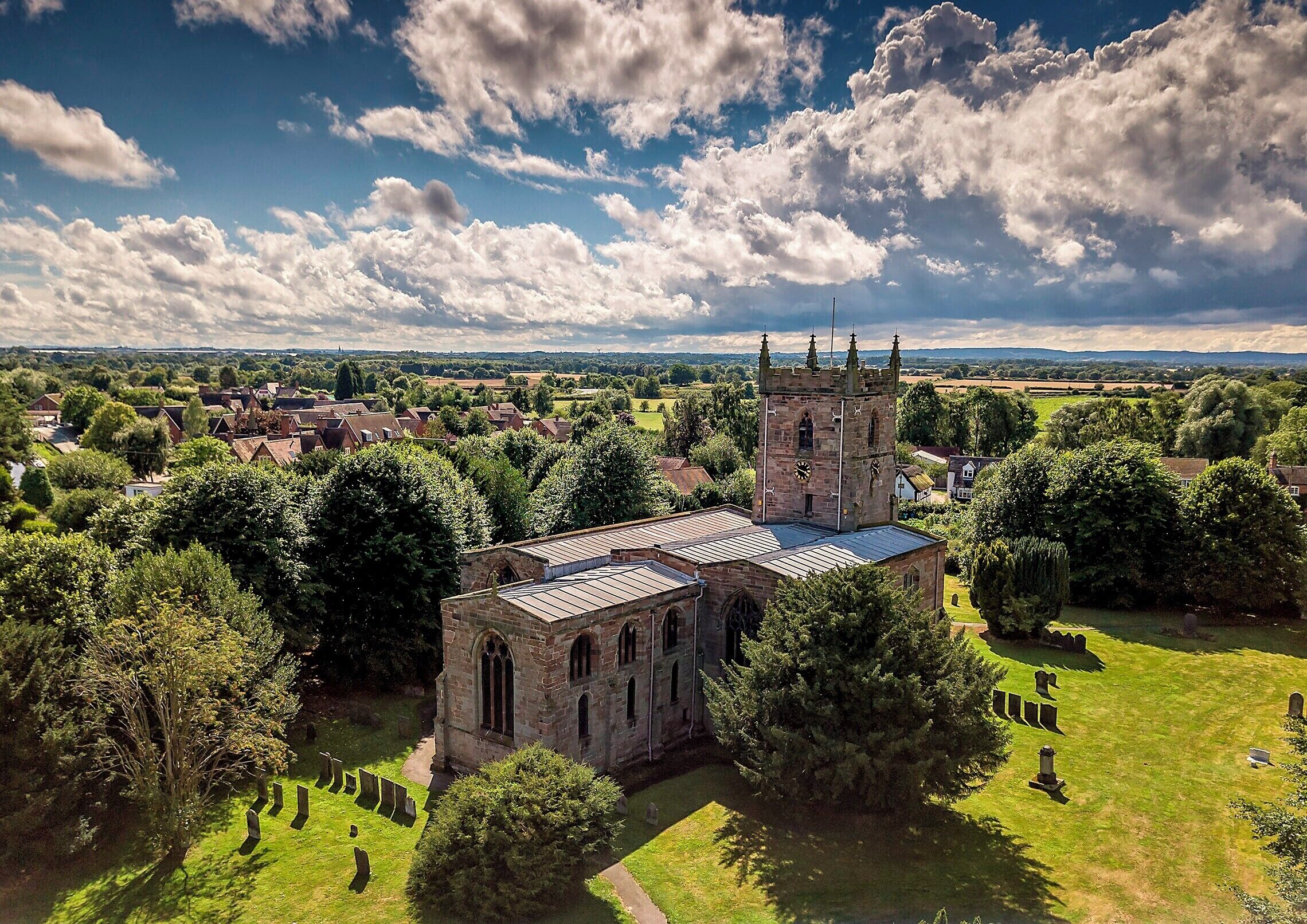 A historic church with a tower, surrounded by a cemetery and lush greenery.