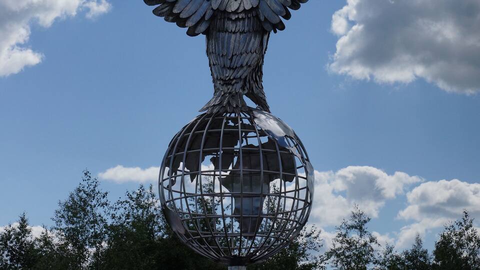 A large metal sculpture of an angel with outstretched wings and a globe at its feet.