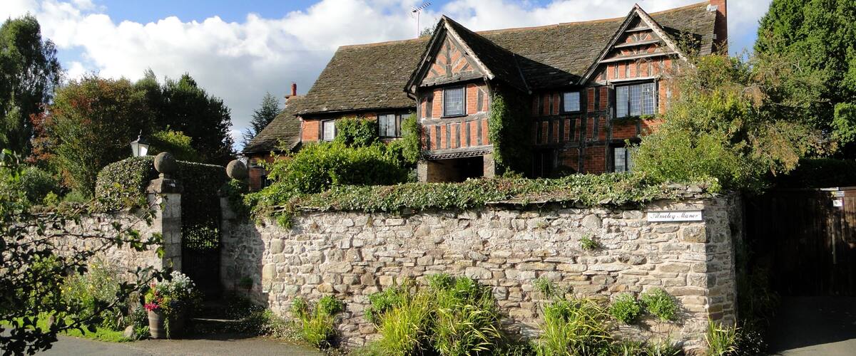 A traditional stone wall with a gate, flanked by lush greenery and a stone lamp post.