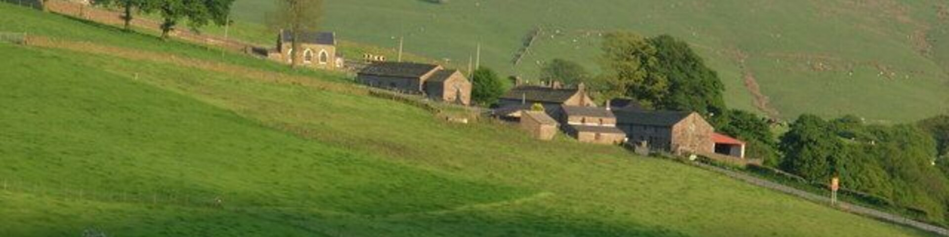 Un paisaje rural con colinas ondulantes, un pequeño grupo de casas y cielo despejado.