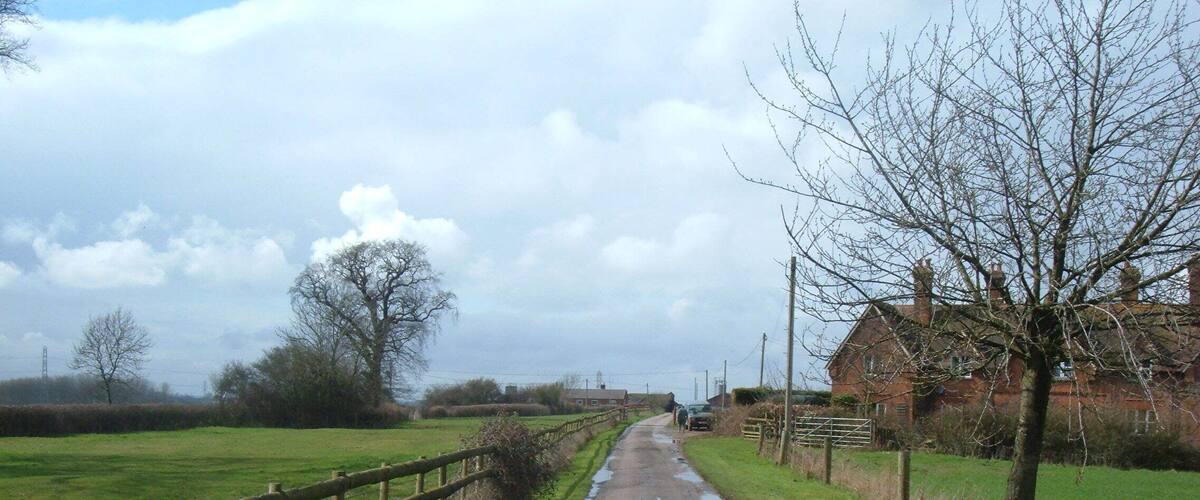 A rural road with a wooden fence on one side and a brick house on the other.