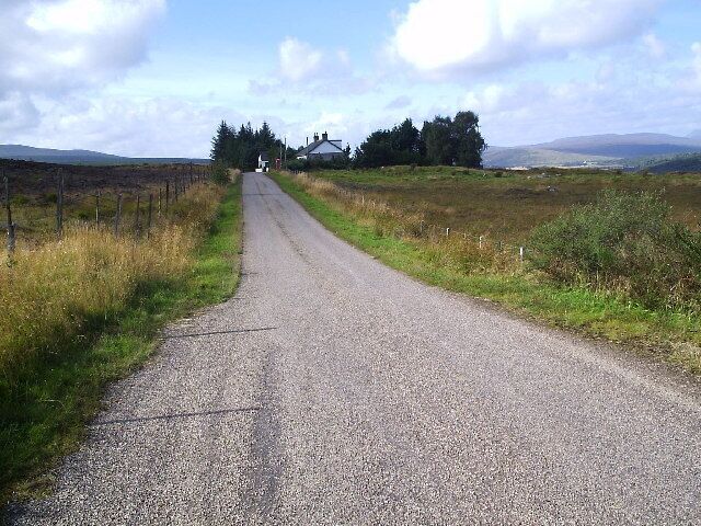 A rural road with a fence on one side and open fields on the other.