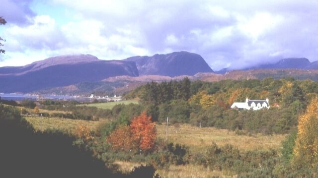 A white house surrounded by autumn-colored trees and mountains in the background.