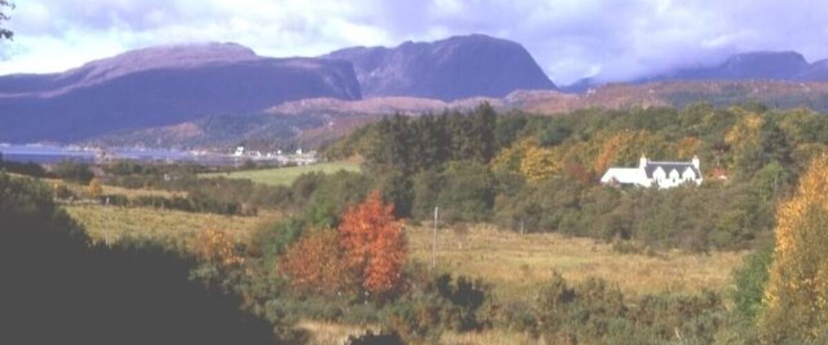 A white house surrounded by autumn-colored trees and mountains in the background.