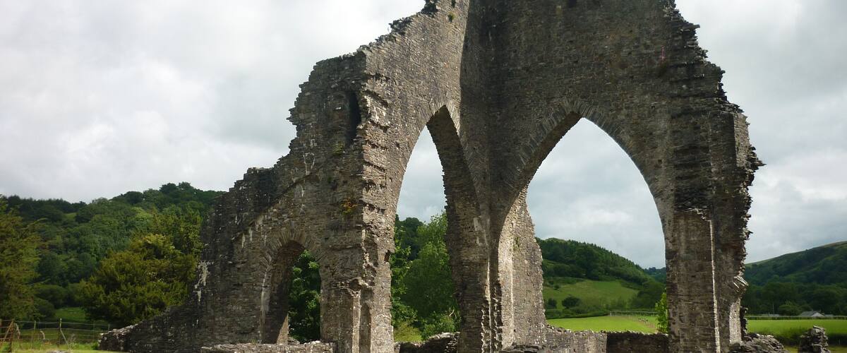 The ruins of a medieval stone archway amidst a lush green landscape.