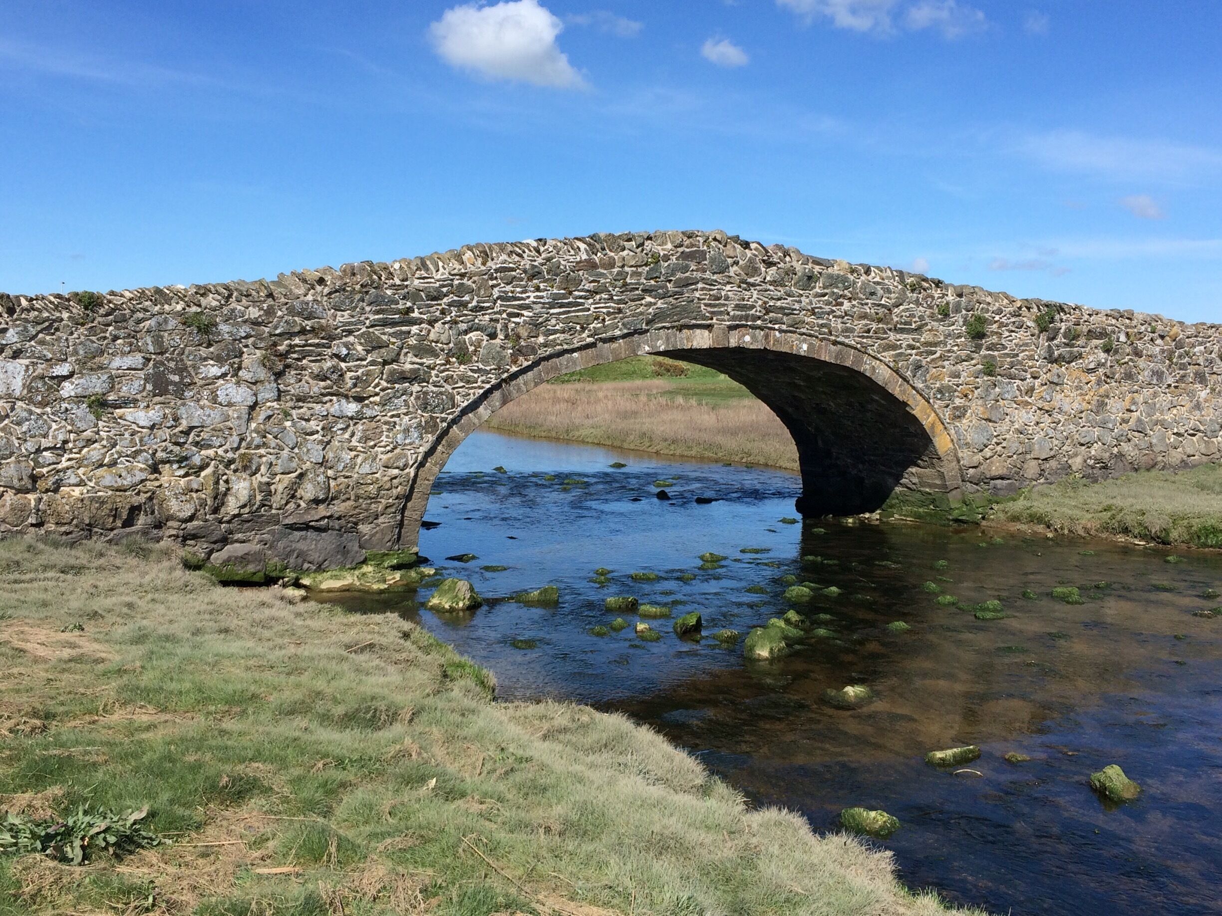 A stone bridge over a river with grass and rocks around.