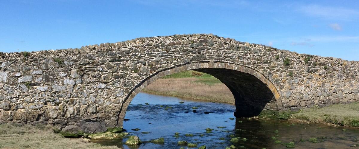 A stone bridge over a river with grass and rocks around.