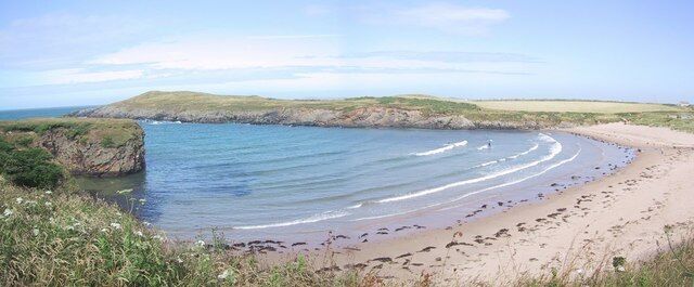 Una playa costera con olas suaves, una orilla arenosa y dunas cubiertas de hierba.