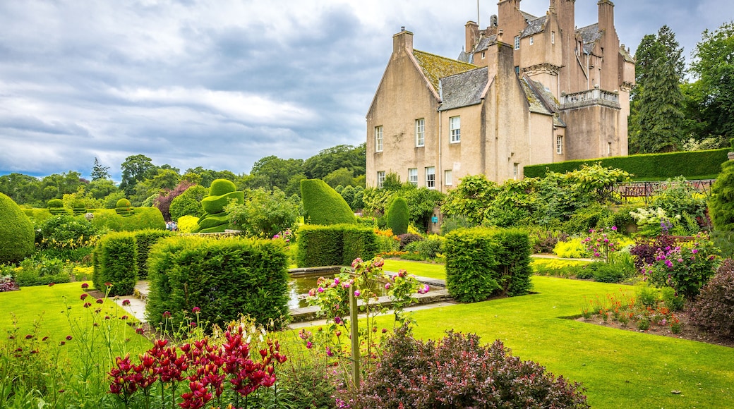 A historic building with a well-manicured garden, including hedges, flowers, and a pond.