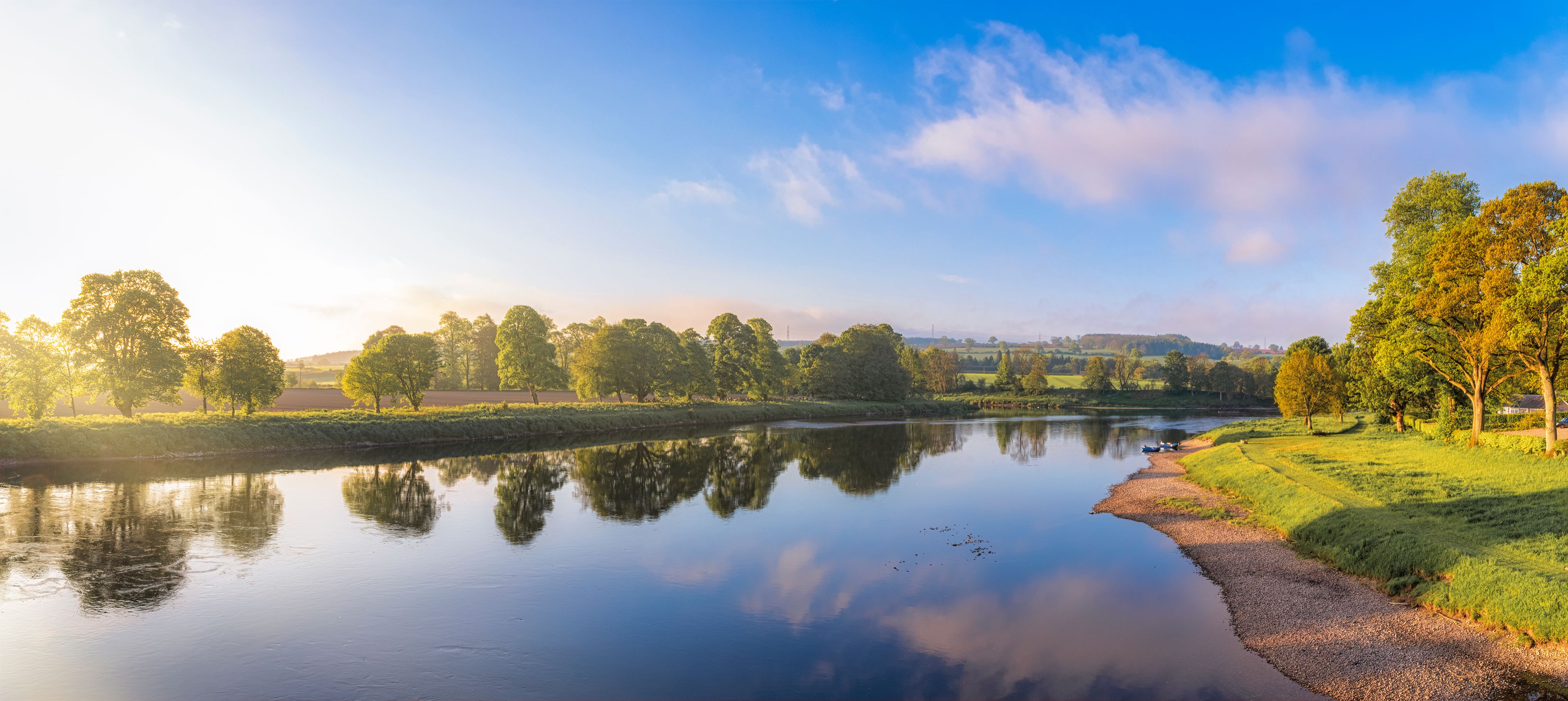 Un río tranquilo que refleja árboles y un cielo despejado.