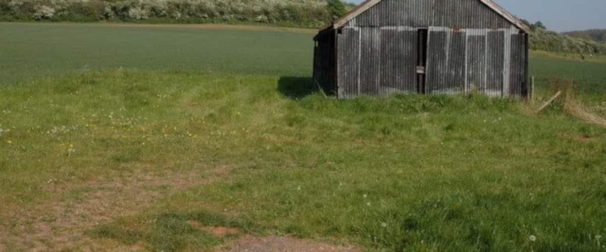 A rustic wooden barn in a grassy field with a clear sky.