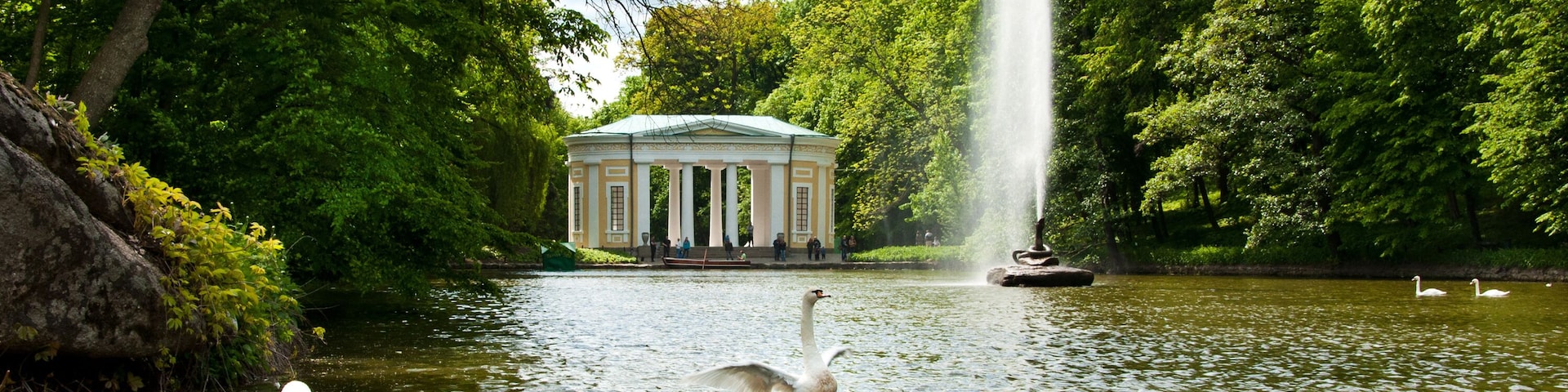 Un cisne en un lago con una fuente y un edificio clásico al fondo.