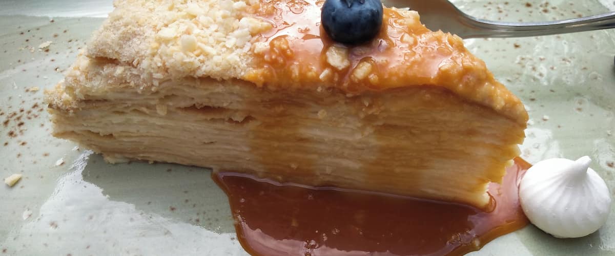 A slice of layered pastry with a blueberry and a dollop of cream on a ceramic plate.