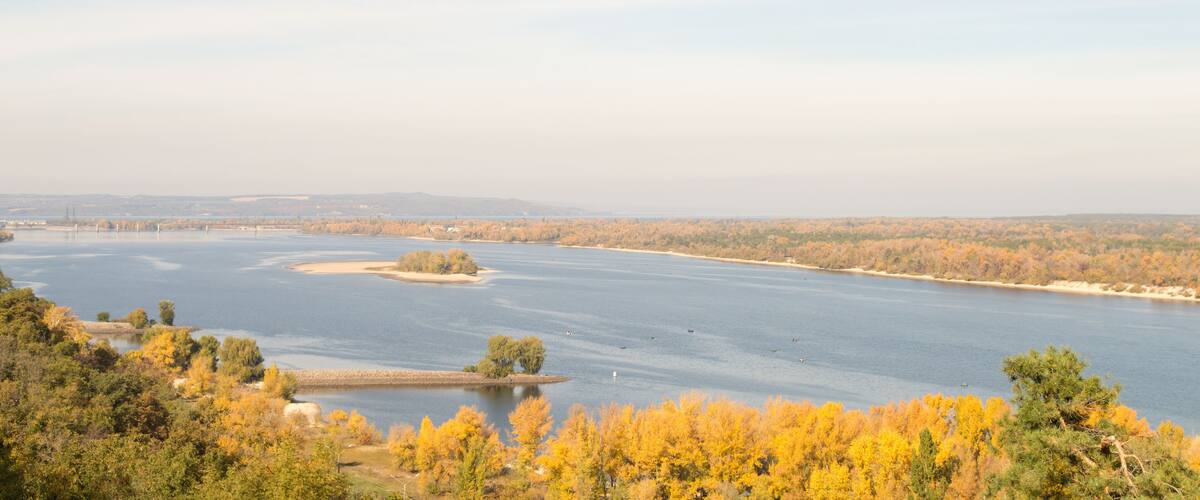 A river with autumn foliage, a bridge, and distant hills.