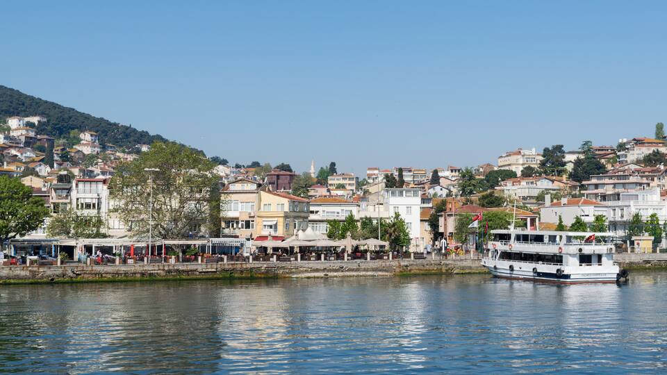 A waterfront cityscape with a boat docked near the shore, surrounded by buildings and trees.