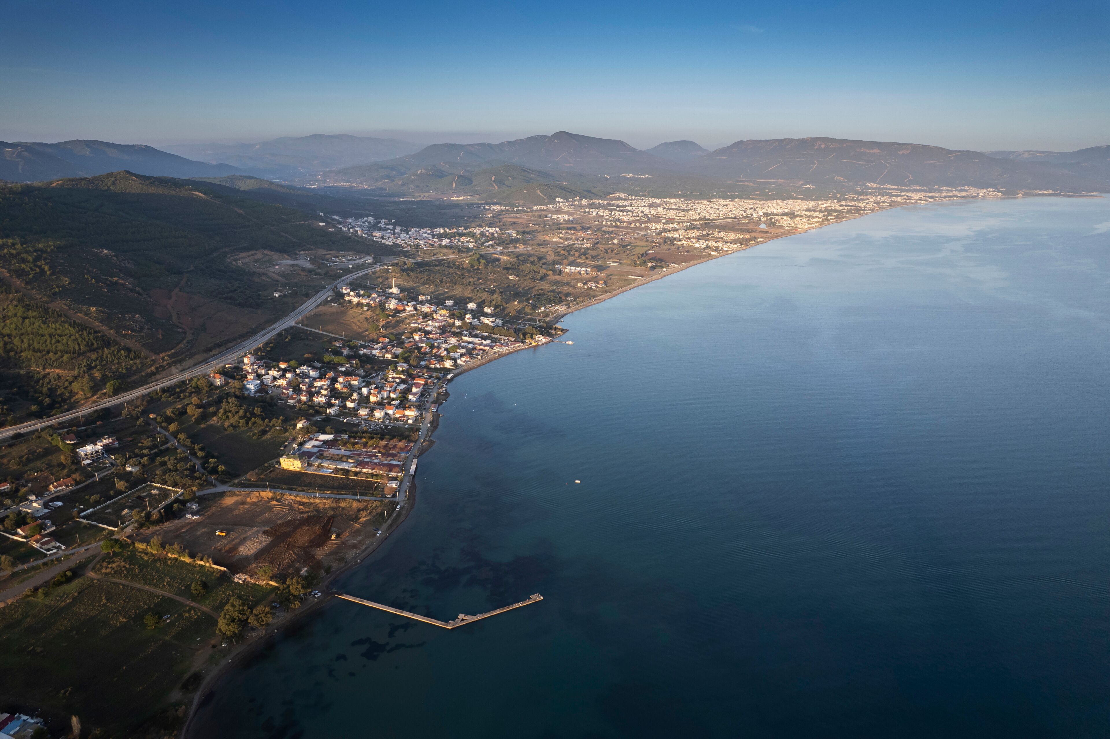 An aerial view of a coastal town with a harbor, mountains in the background, and a clear sky.