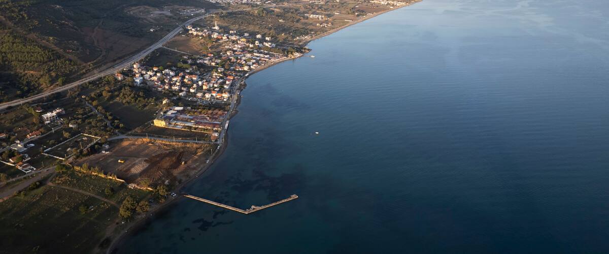 An aerial view of a coastal town with a harbor, mountains in the background, and a clear sky.