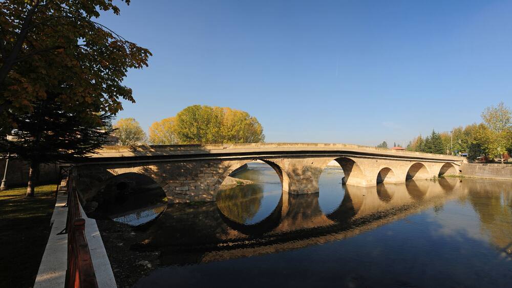 Un pont de pierre enjambe une rivière paisible, et les arbres se reflètent dans l’eau.