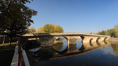 A stone bridge over a calm river with trees reflecting on the water.