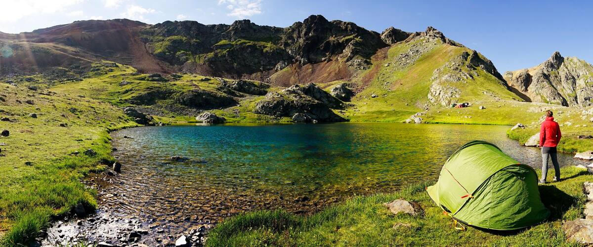 A green tent near a clear lake surrounded by mountains.