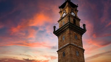 A clock tower with a balcony, set against a sunset sky.
