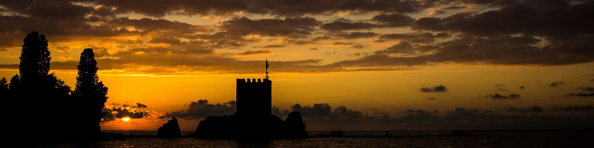 A sunset over a coastal landscape with a prominent castle silhouette and rocky outcrops.