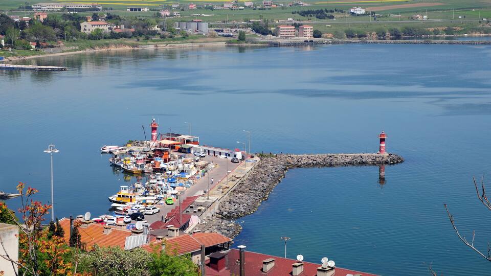 A harbor with boats, a lighthouse, and buildings along the shore.