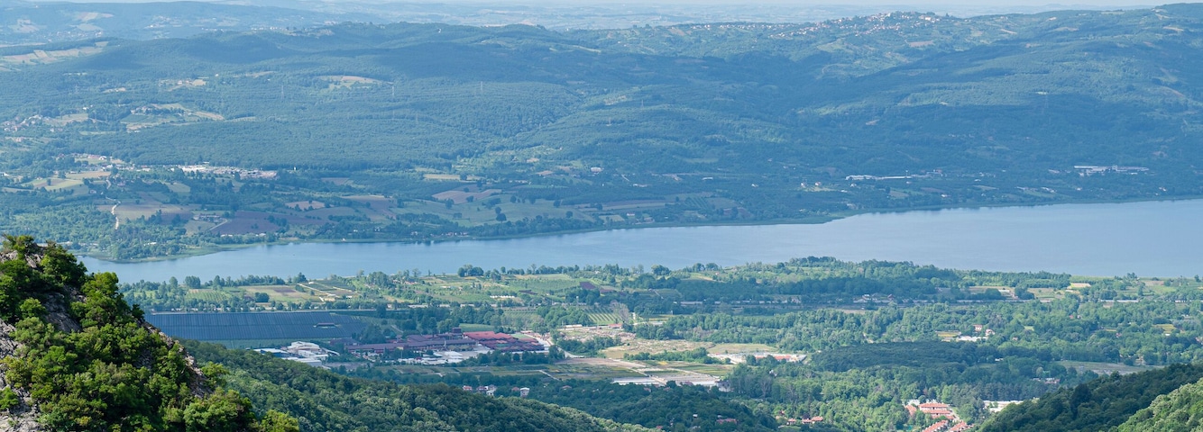 Un paisaje montañoso con bosques densos, un lago y edificios a lo lejos.