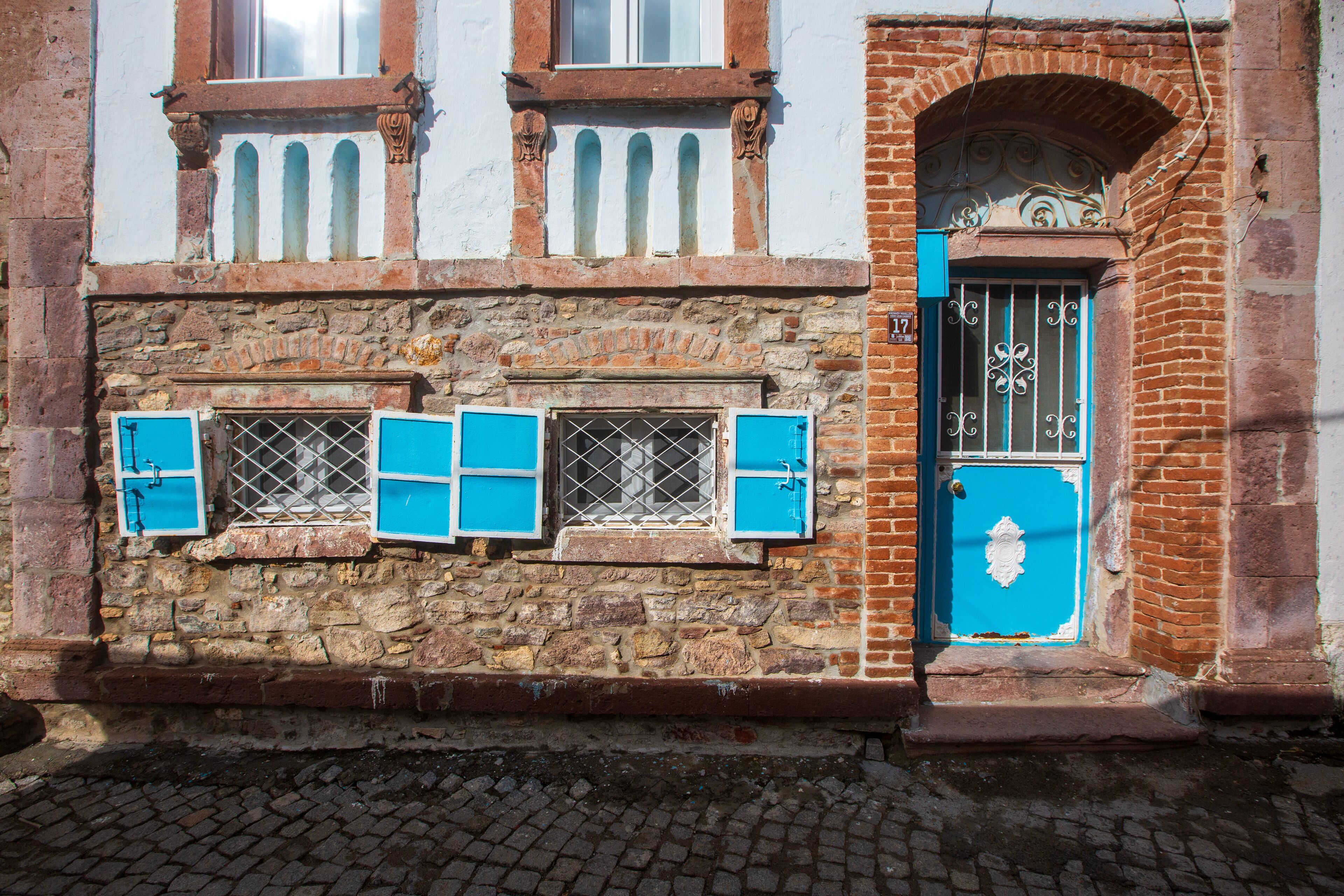 A historic building with a stone facade, blue shutters, and a blue door with decorative ironwork.