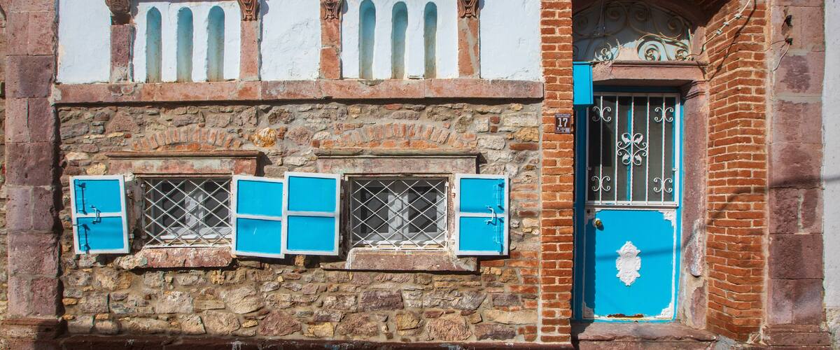 A historic building with a stone facade, blue shutters, and a blue door with decorative ironwork.