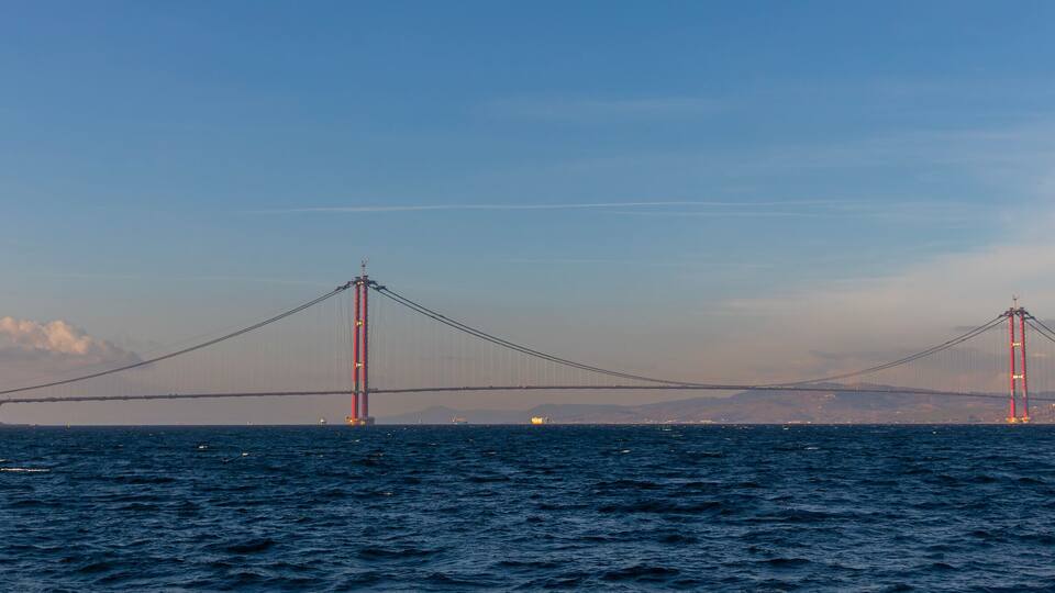 A suspension bridge over a body of water with a city skyline in the background.