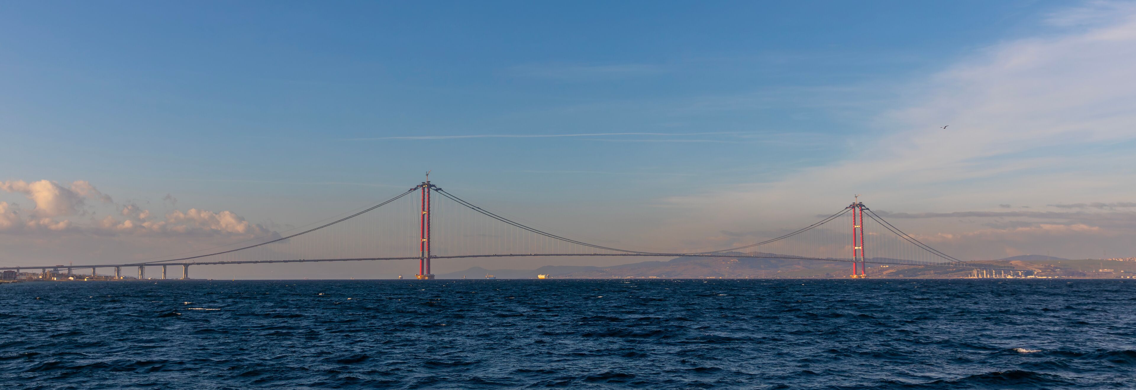 A suspension bridge over a body of water with a city skyline in the background.