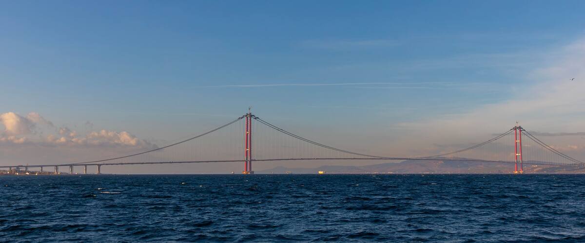 A suspension bridge over a body of water with a city skyline in the background.