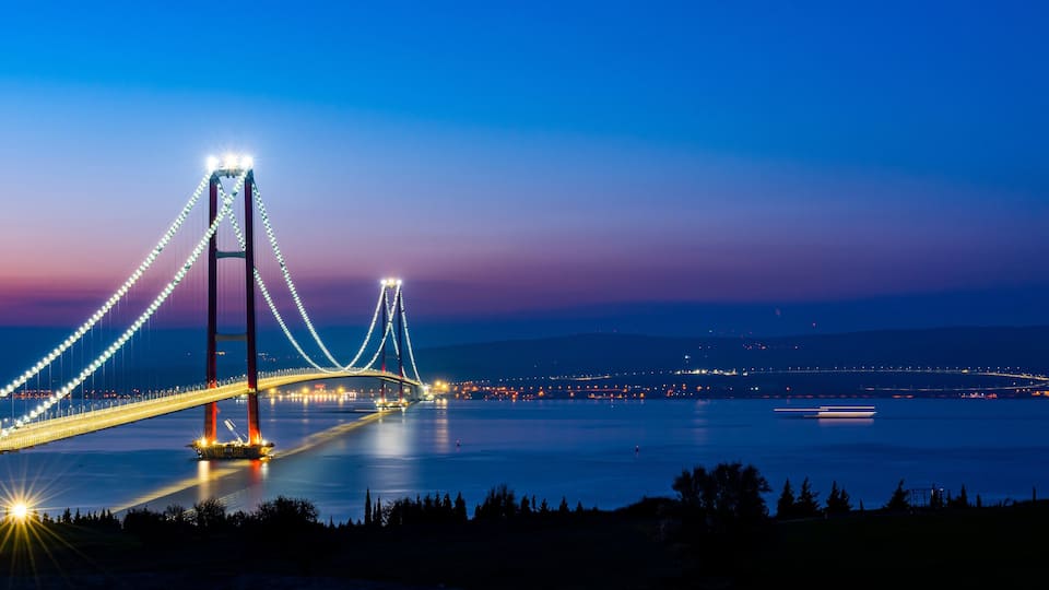 A bridge at dusk with lights reflecting on the water.